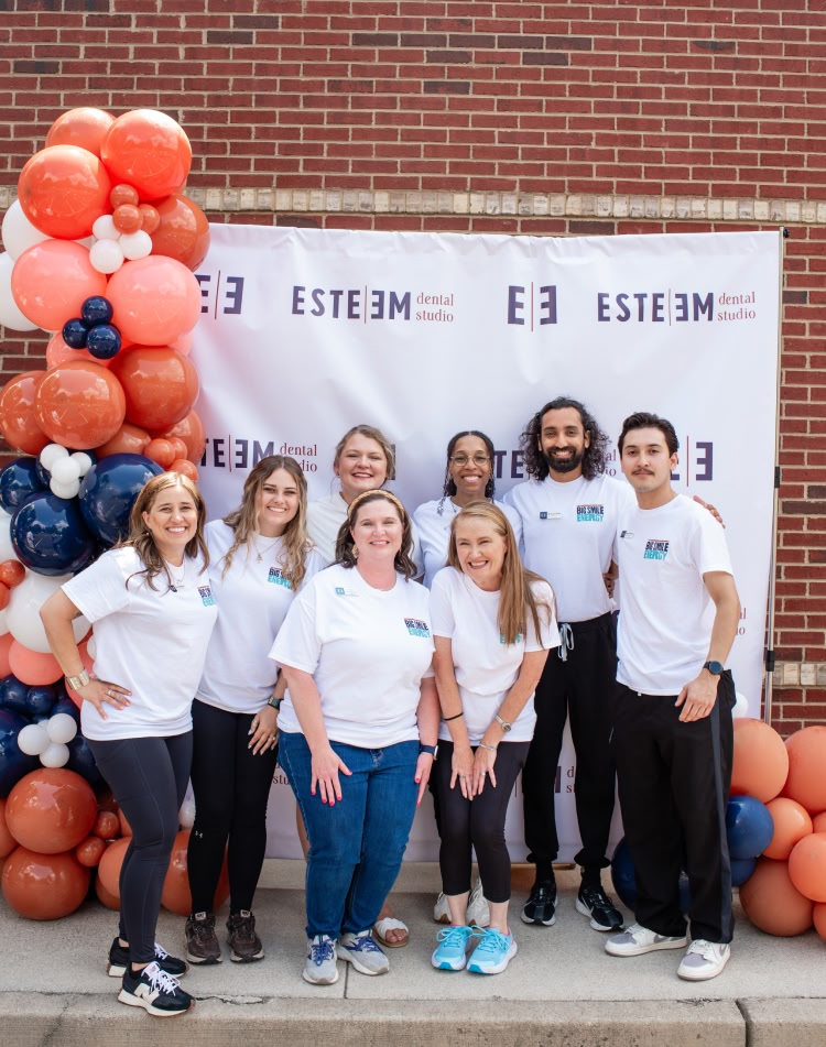 A young man smiling down at his phone while sitting on his couch scheduling a dental appointment at esteem dental studio